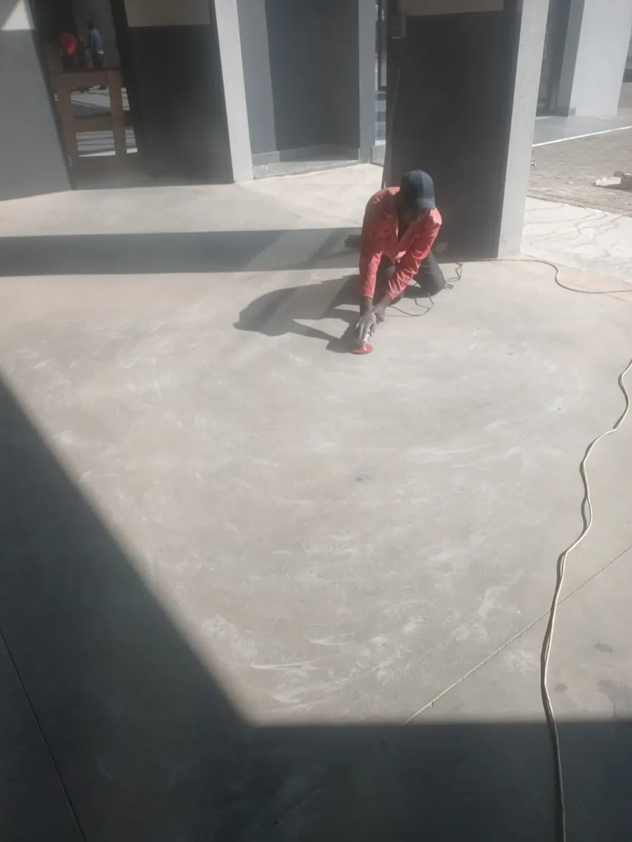 Installer kneeling on a bare concrete slab, preparing the surface with a power tool before coating