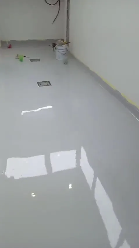 Light-grey gloss epoxy floor in a narrow room with two floor drains, masking tape still on the wall edges