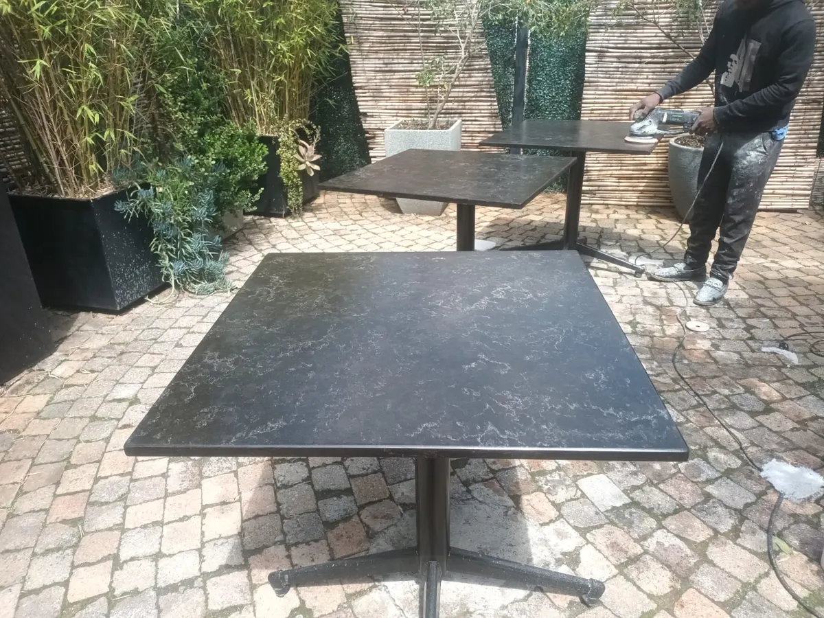Installer polishing a dark stone outdoor table with a hand polisher