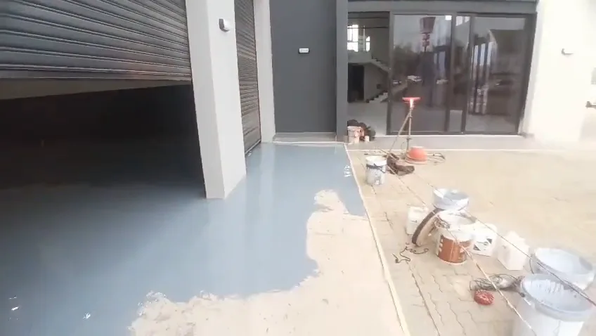 Fresh grey epoxy running out to the roller door of a commercial unit, with tins and a mixing drill on the paving outside